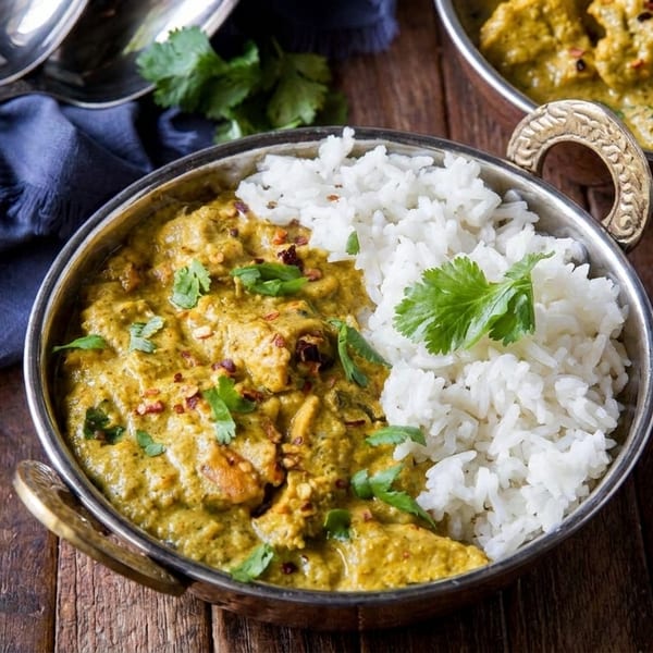 Two bowls of green curry with white rice and cilantro on a wooden table.